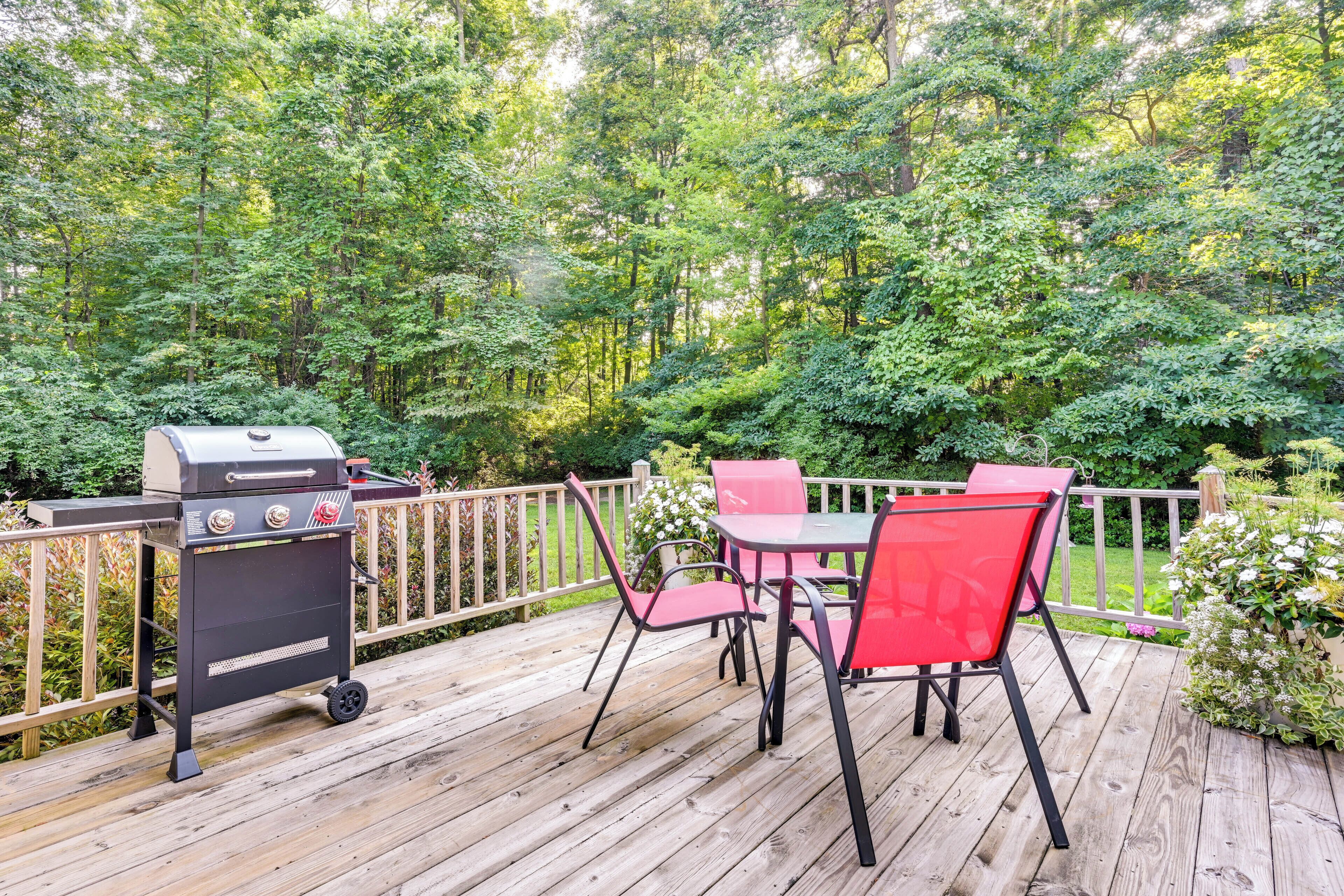 A wooden deck with a grill and red chairs.