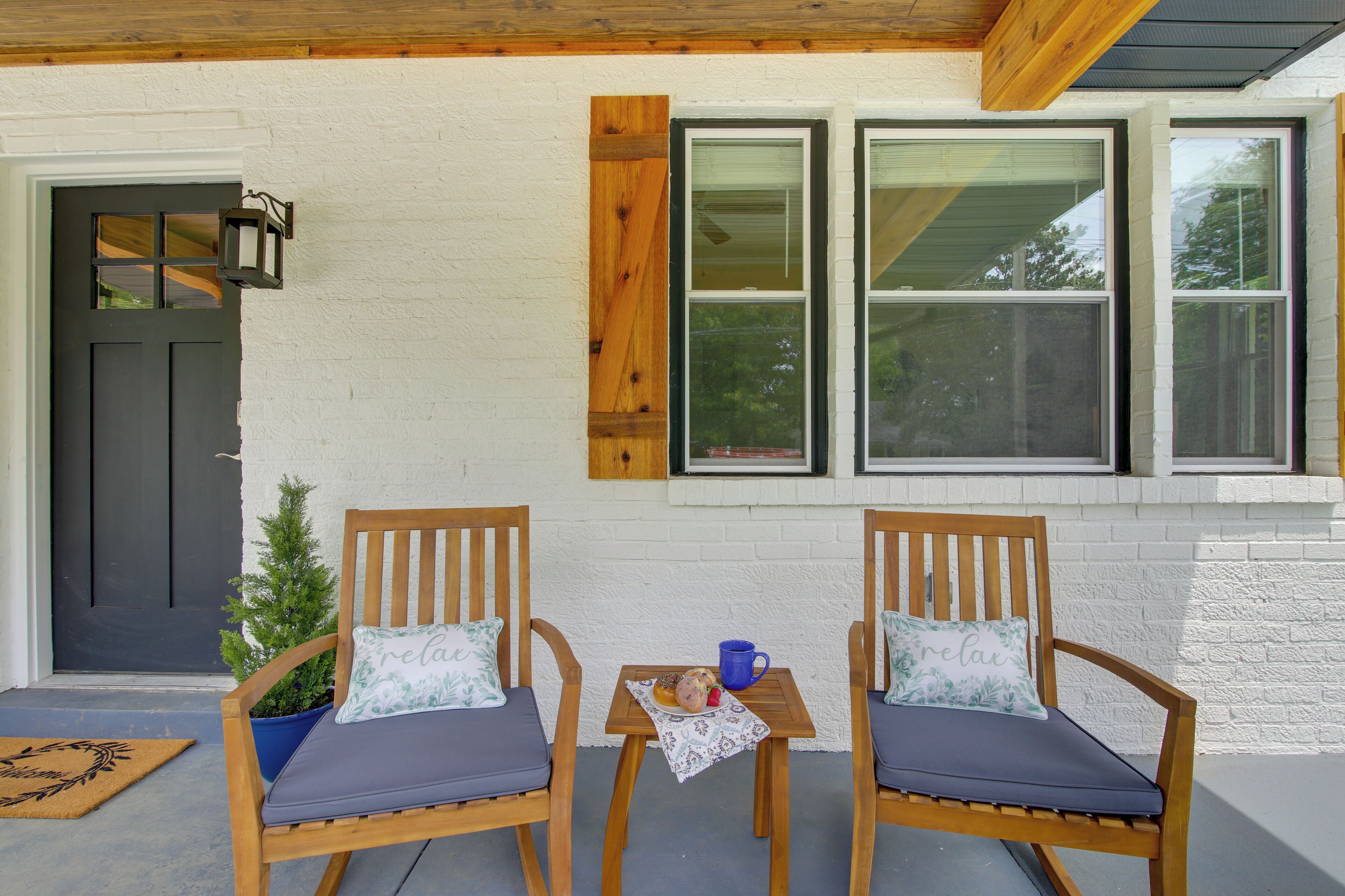 A porch with two wooden chairs, a small table with a blue mug, and a potted plant.