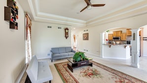 A spacious living room with a sofa, coffee table, and a large rug. A ceiling fan is visible, and the room leads to a kitchen area. - Charming Pennsylvania Retreat w/ Deck & Fireplace! (Willow Street)