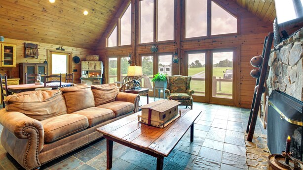 A spacious living room with a wooden ceiling, large windows, a fireplace, and a cozy seating area. - 12 Mi to Staunton River: Nathalie Cabin w/ Deck (Nathalie)