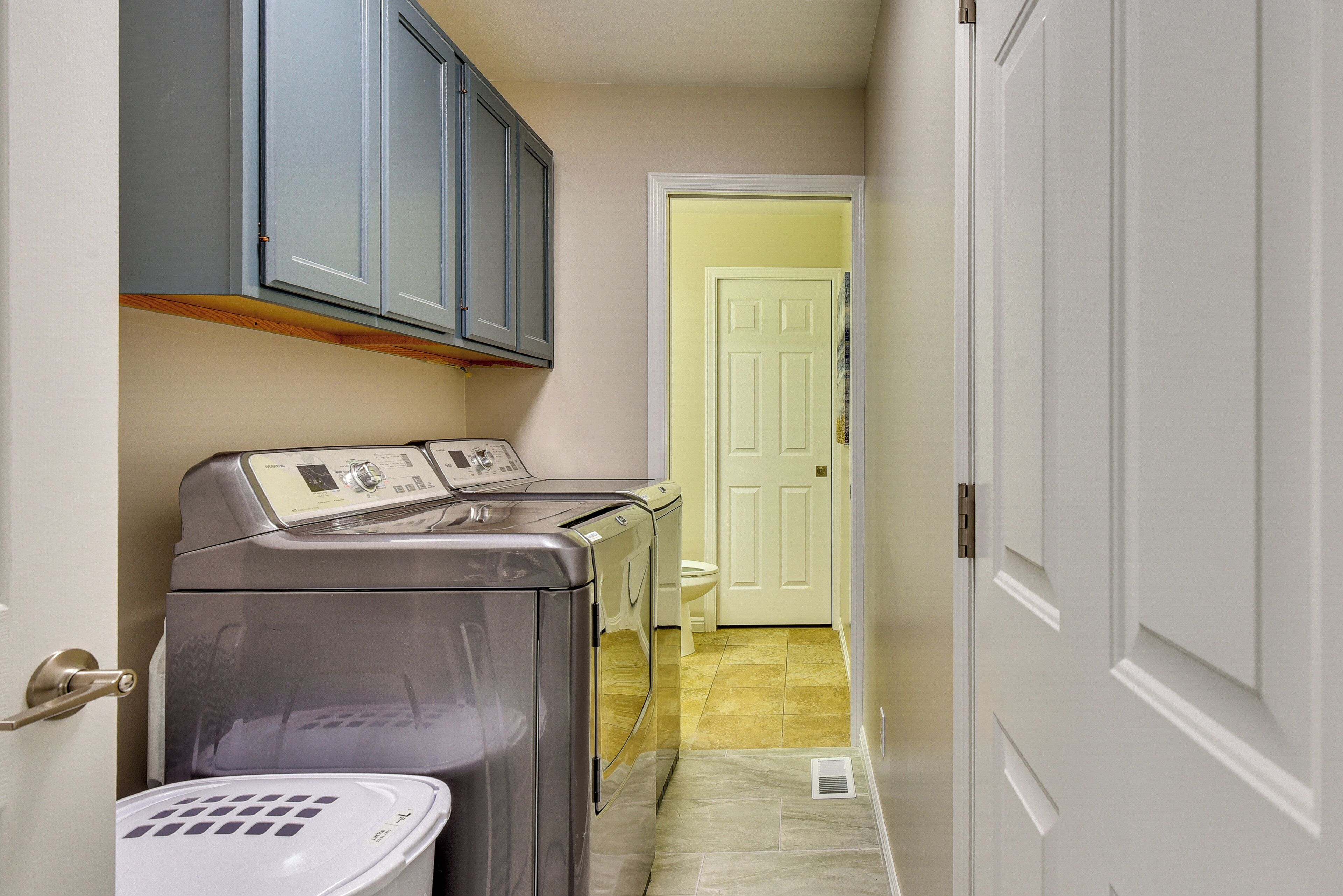 A laundry room with a front-loading washer and dryer, a small sink, and a door leading to another room.