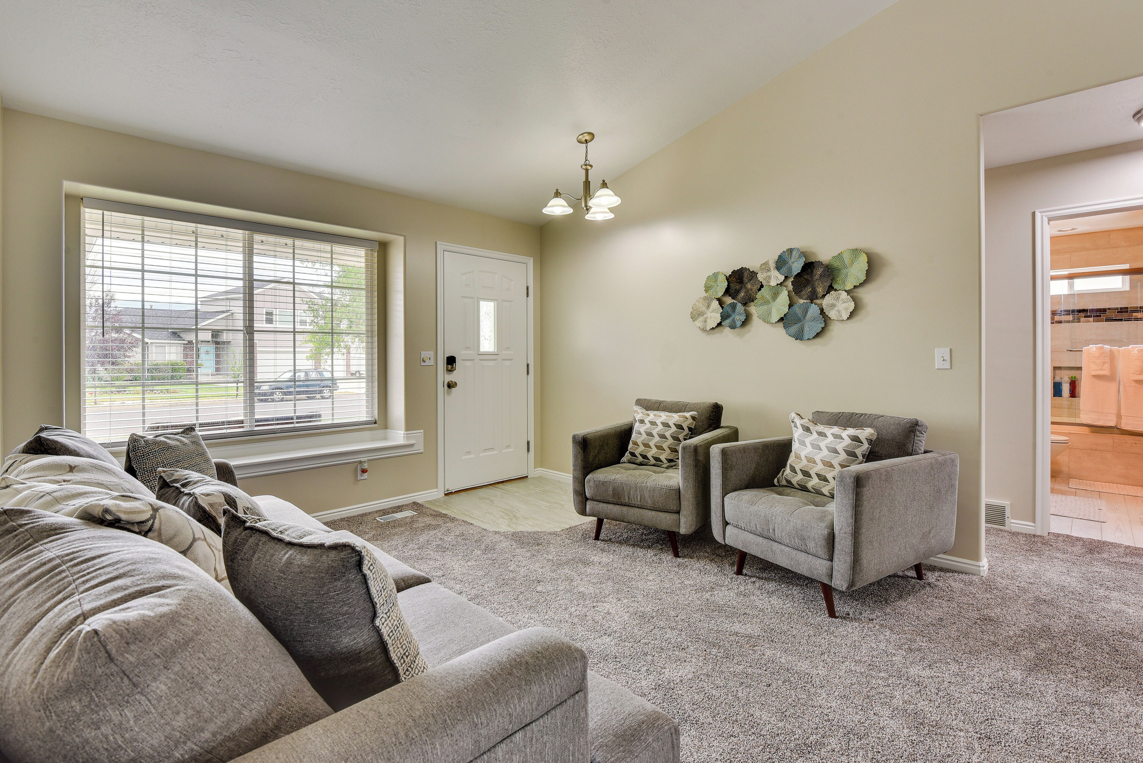 A living room with a large window, two armchairs, a sofa, and a decorative wall piece.