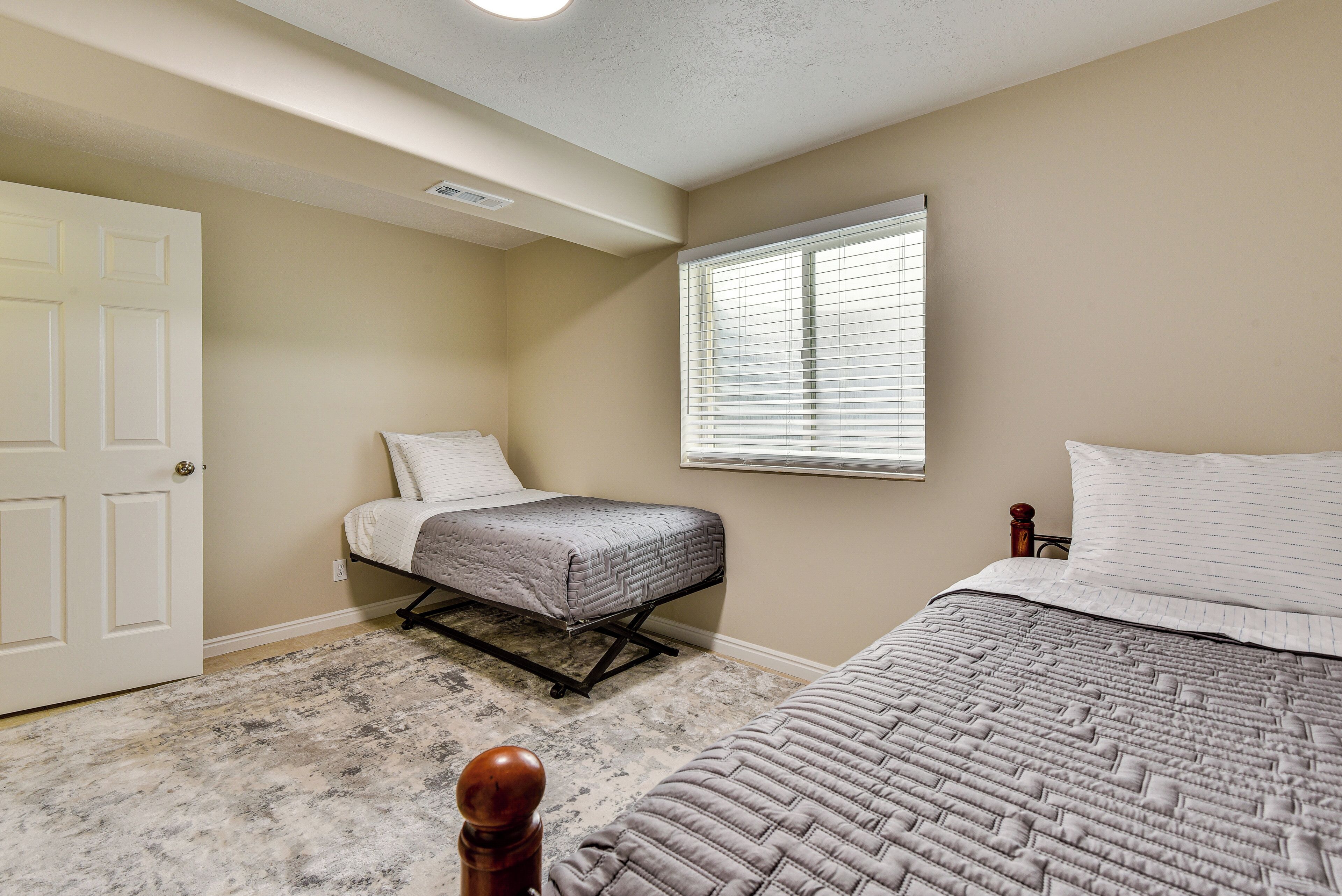 A bedroom with two beds, a door, a window, and a ceiling vent.