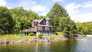Una casa junto al lago con terraza, mobiliario exterior y muelle.