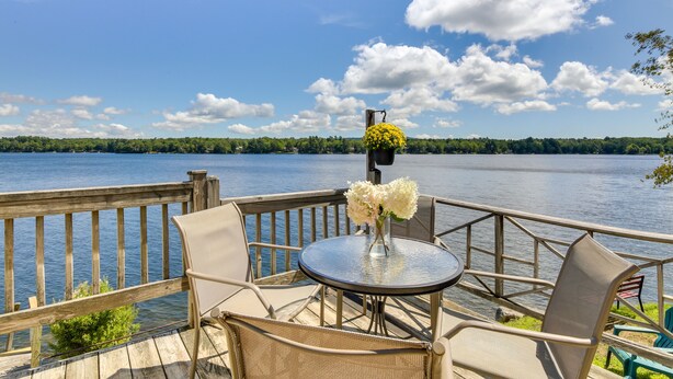 Una terraza con una mesa redonda y sillas, con vista a un lago y una baranda de madera.