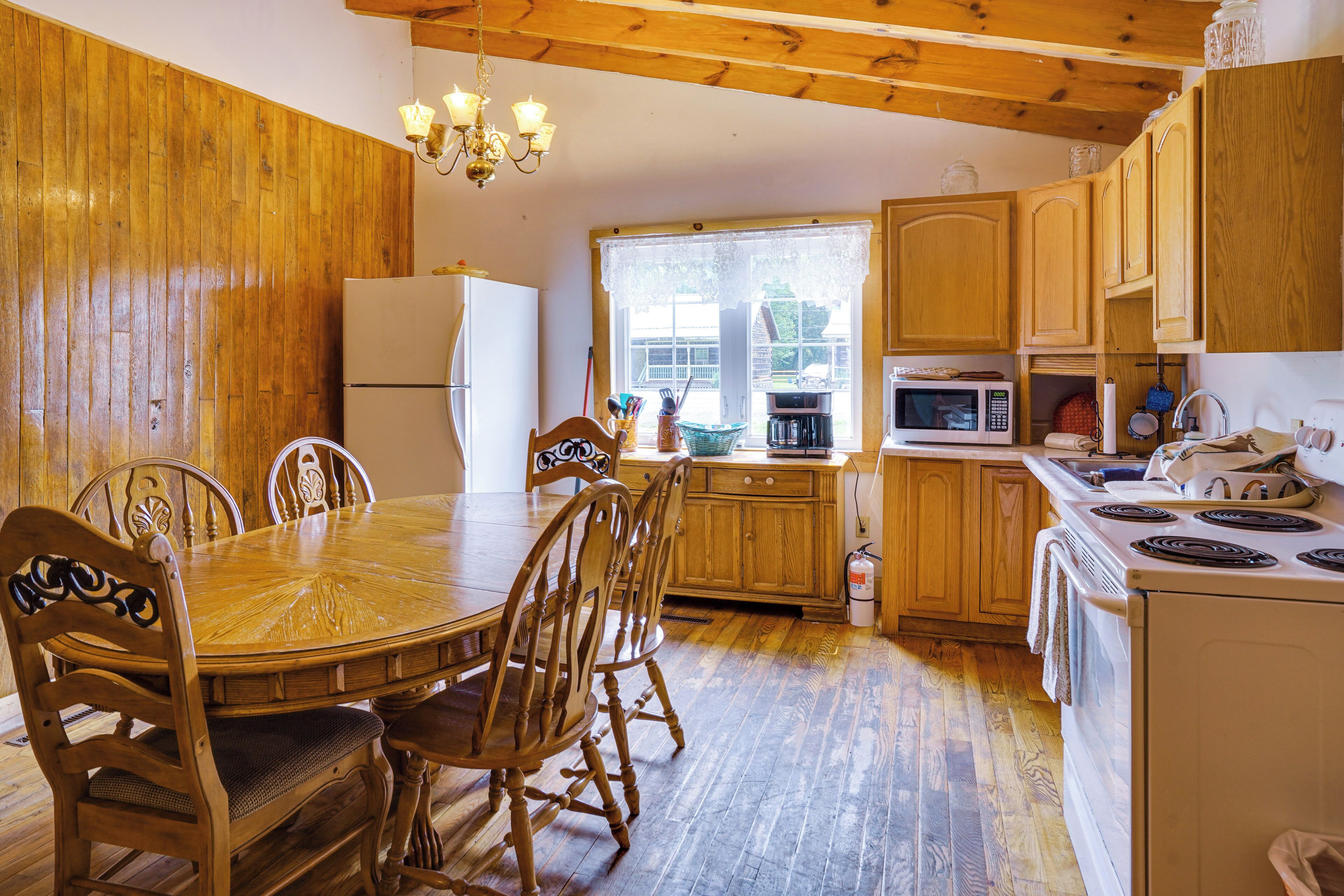 A wooden interior with a dining table, chairs, a refrigerator, a microwave, and a stove.