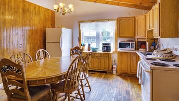 A wooden interior with a dining table, chairs, a refrigerator, a microwave, and a stove.
