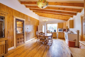 A wooden interior with a dining table, chairs, a chandelier, wooden cabinets, and a kitchen area with appliances. - Historic Cabin Retreat ~ 2 Mi to Seneca Rocks! (Seneca Rocks)