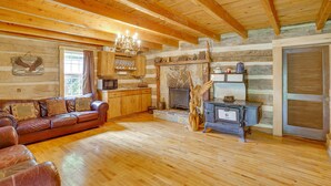 A log cabin interior with a wooden floor, leather sofa, wooden cabinets, a stone fireplace, and a vintage stove. - Historic Cabin Retreat ~ 2 Mi to Seneca Rocks! (Seneca Rocks)