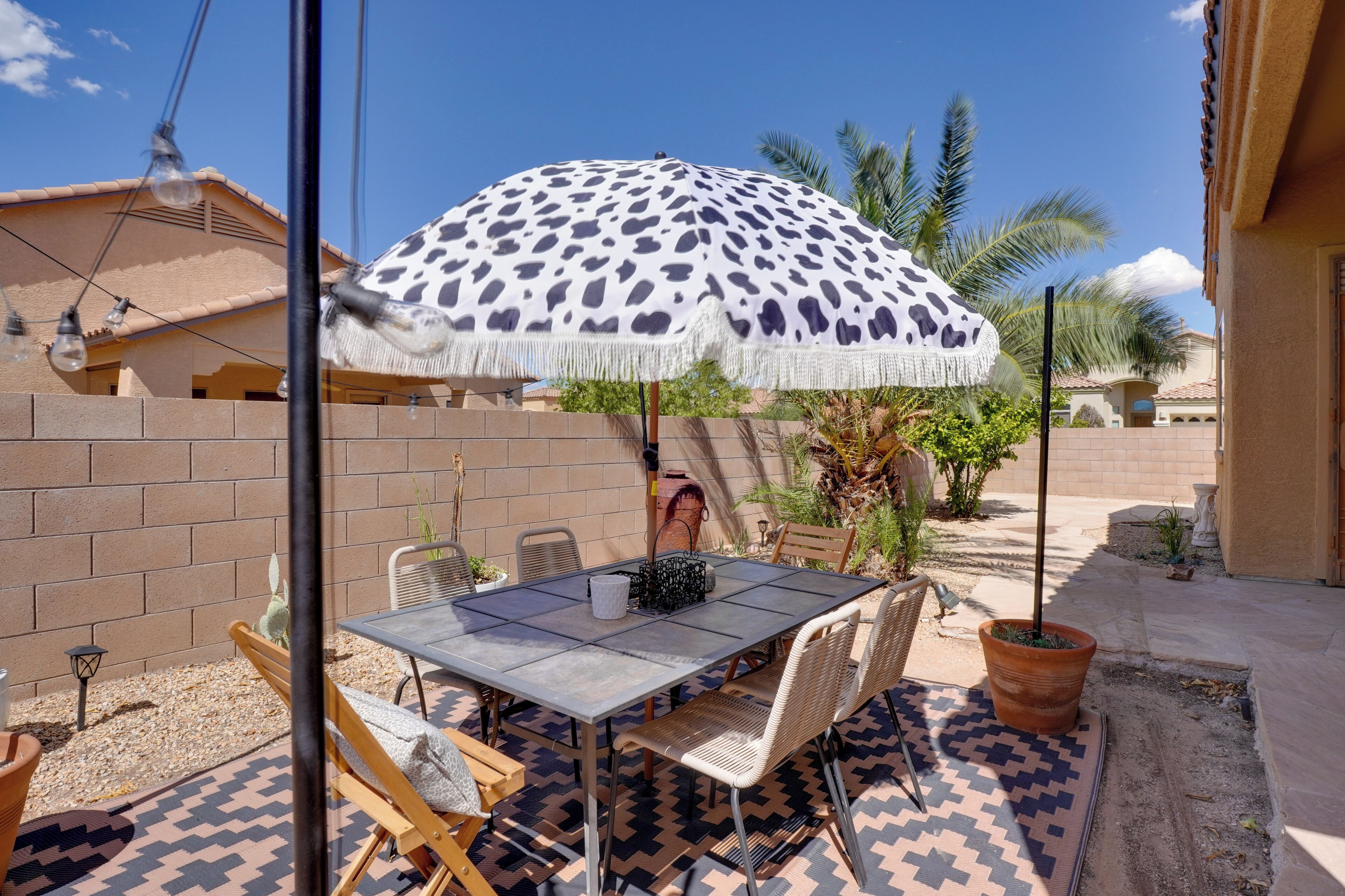 Eine Terrasse im Freien mit Tisch, Stühlen, einem gemusterten Teppich und einem großen Sonnenschirm.