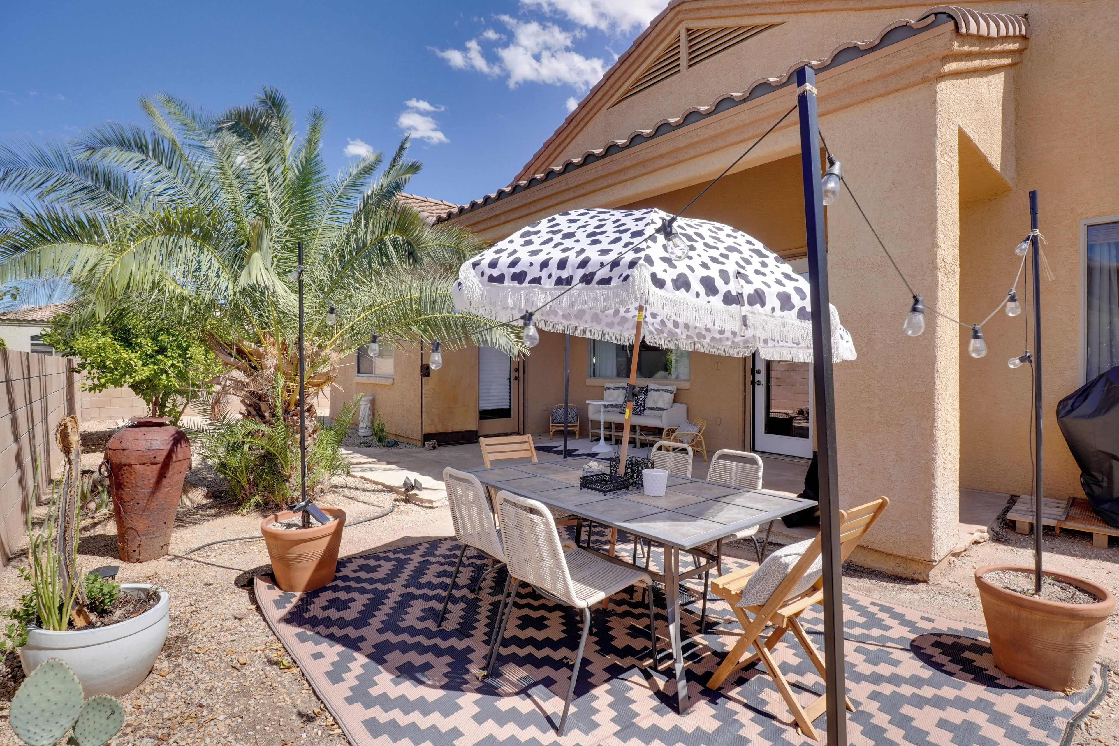 An outdoor patio with a table and chairs, a patterned rug, and a large umbrella.