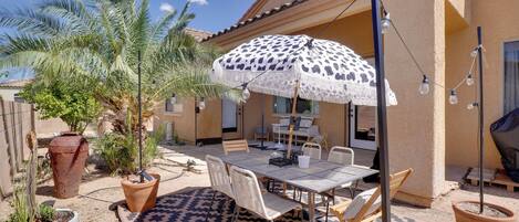 An outdoor patio with a table and chairs, a patterned rug, and a large umbrella.
