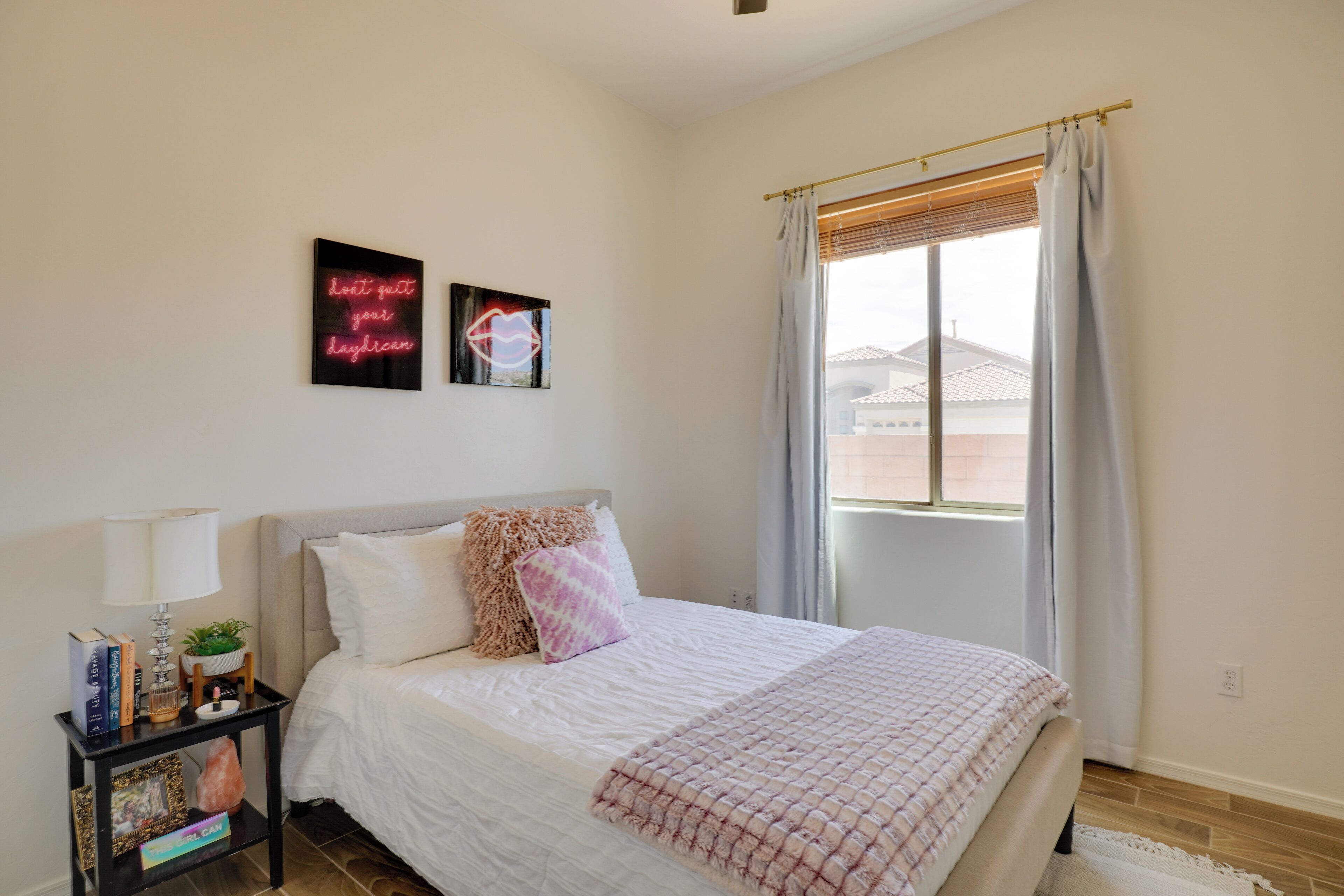 A bedroom with a bed, a bedside table with a lamp, a small plant, and two framed pictures on the wall.