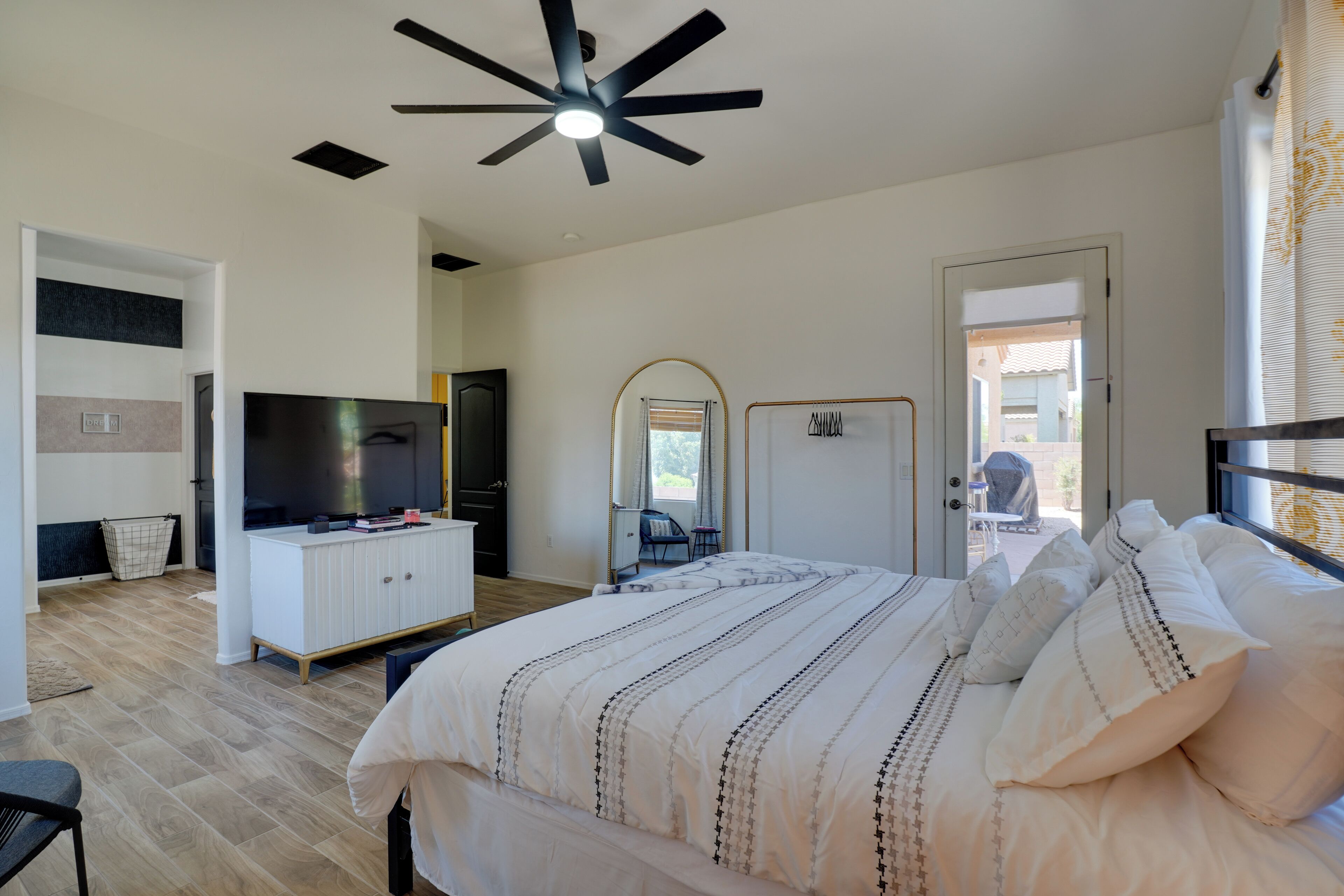 Une chambre à coucher comprenant un lit, un téléviseur, un ventilateur de plafond et une porte donnant sur un balcon.