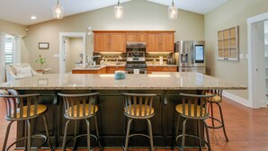 A kitchen with a large island, bar stools, wooden cabinets, stainless steel appliances, and pendant lighting.