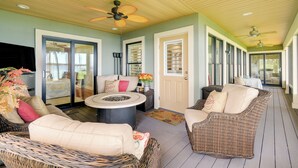 A covered outdoor seating area with wicker furniture, a round table, and ceiling fans.