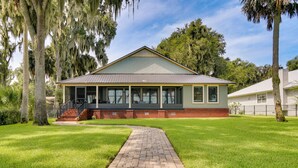 A single-story house with a brick foundation and a gabled roof, surrounded by a well-maintained lawn and trees.