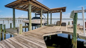 A wooden dock with a covered seating area, a boat docked at the pier, and calm water in the background.