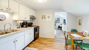 Eine moderne Küche mit weißen Schränken, Edelstahlgeräten und Holzboden. Es gibt einen Essbereich mit Tisch und Stühlen, sowie eine Sitzecke im Hintergrund.