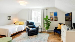 Ein gemütliches Zimmer mit einem Bett, einem schwarzen Ledersessel, einem kleinen Tisch, einer Pflanze und einem Fernseher.