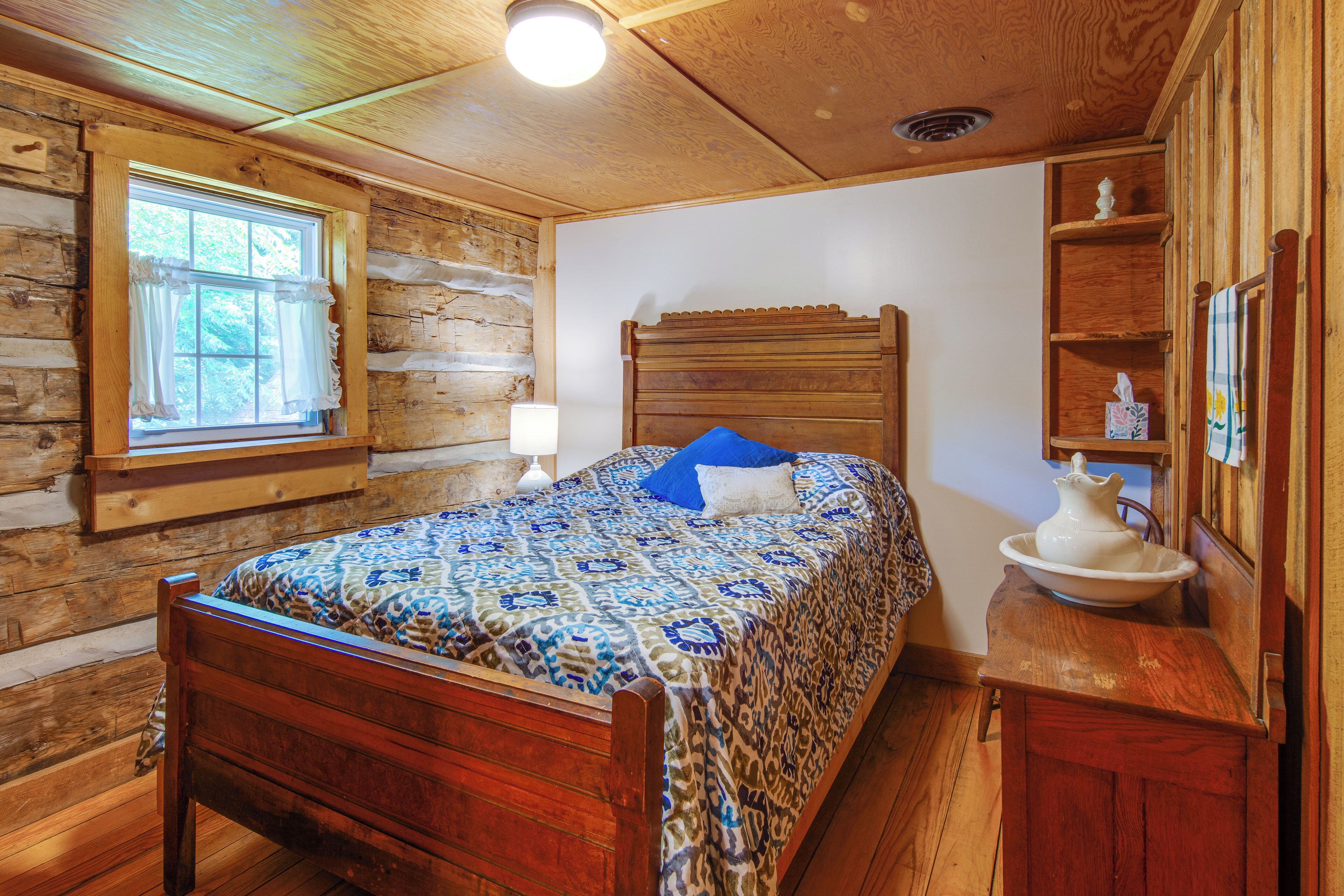 A wooden log cabin bedroom with a bed, a window, a nightstand, and a shelf with decorative items.