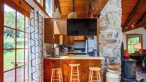 A rustic kitchen with wooden cabinets, a stone wall, and a large window overlooking a garden. - Historic Morrisdale Area Cabin w/ Deck & Fireplace (Morrisdale)