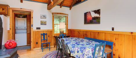 A wooden interior with a dining table, chairs, a stove, and a window.
