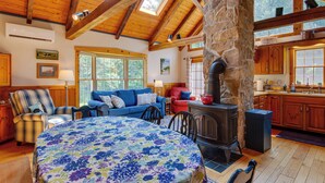 A cozy cabin interior with a large round table, a blue sofa, a fireplace, and wooden beams. - Historic Morrisdale Area Cabin w/ Deck & Fireplace (Morrisdale)