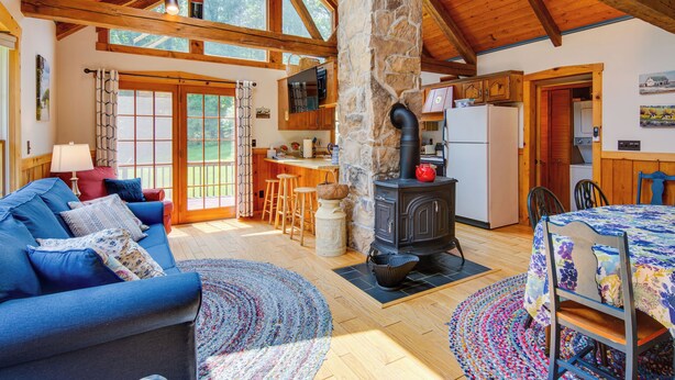 A cozy living room with a blue sofa, a stone fireplace, and a dining area with a table. - Historic Morrisdale Area Cabin w/ Deck & Fireplace (Morrisdale)