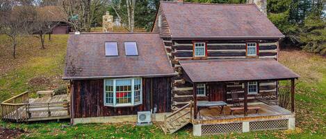 A log cabin with a porch, a chimney, and a small deck.