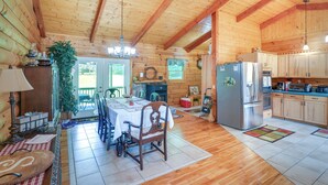 A wooden cabin interior with a dining area, kitchen, and a large window. - Serene Valley Bend Cabin Rental: 7 Private Acres! (Beverly)