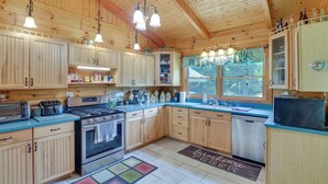 A kitchen with wooden cabinets, stainless steel appliances, and hanging pendant lights. - Serene Valley Bend Cabin Rental: 7 Private Acres! (Beverly)