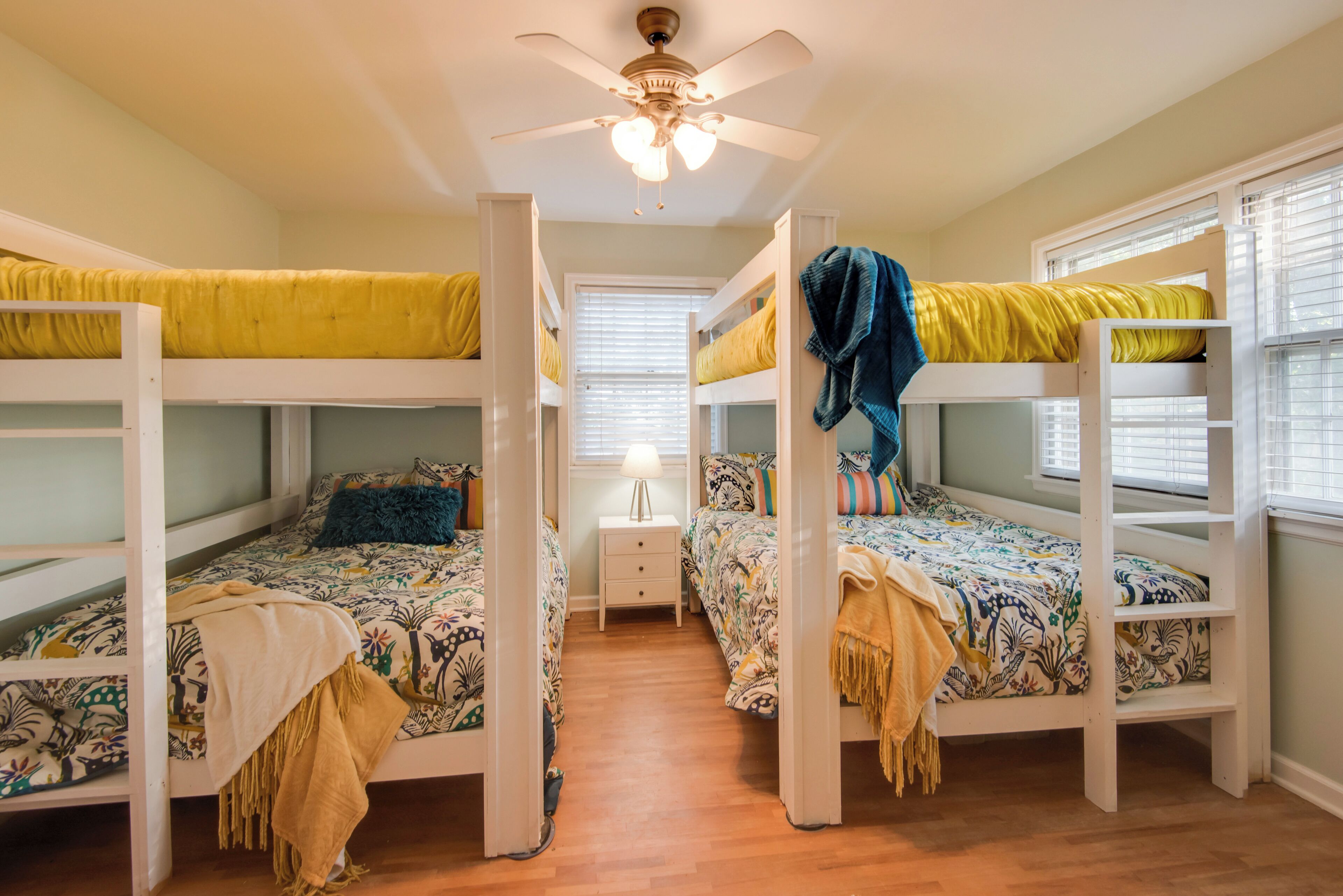 A room with bunk beds, a ceiling fan, and a window with blinds.