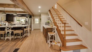 A spacious kitchen with wooden beams, a large island with bar stools, and a wooden staircase. - Charming Villisca Getaway w/ Screened Porch! (Villisca)