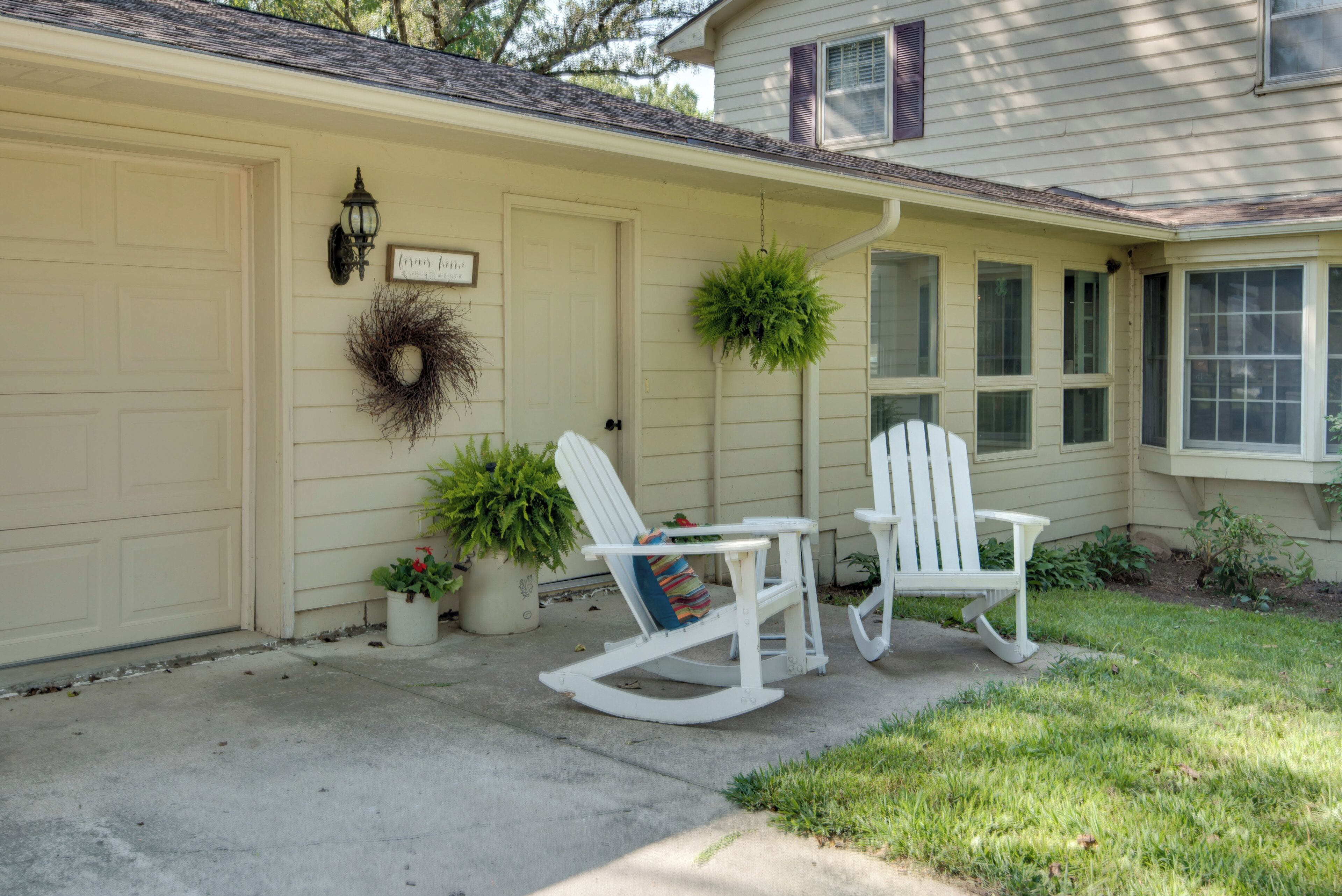 A house with a garage door, a front porch with two rocking chairs, a small table, and potted plants.