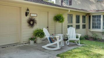 A house with a garage door, a front porch with two rocking chairs, a small table, and potted plants.