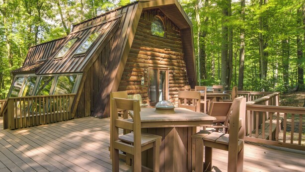 Une cabane en bois dotée d’un toit en pente et de grandes fenêtres, entourée d’une terrasse aménagée avec des meubles en bois.