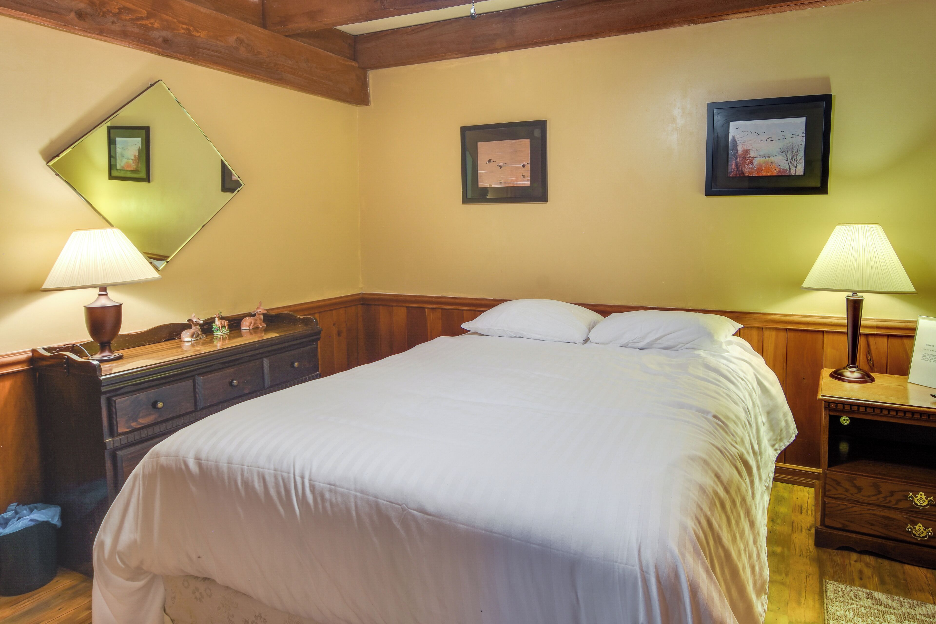 Un dormitorio ordenado con una cama, dos mesitas de noche con lámparas, un aparador y cuadros enmarcados en la pared.