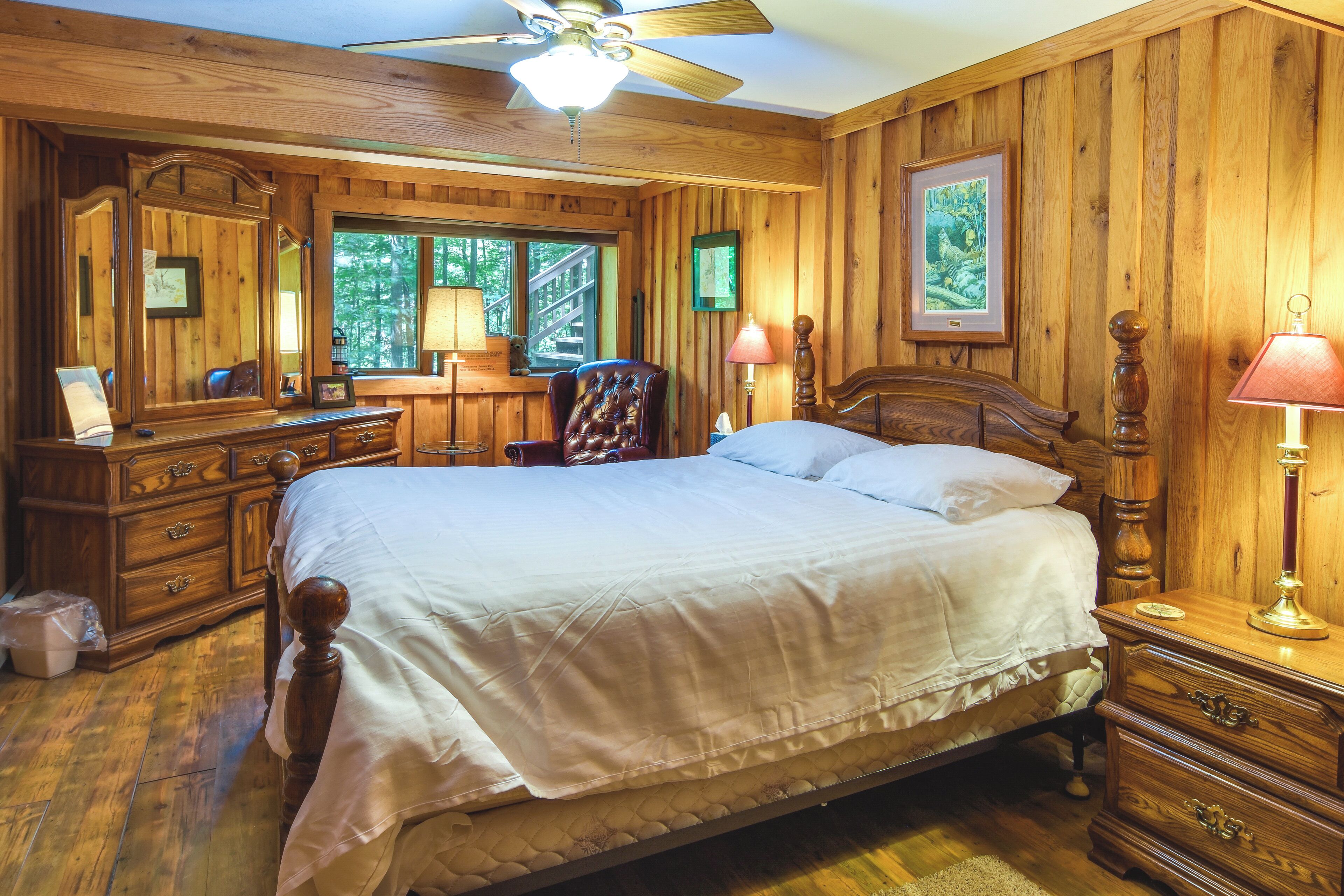 Ein Schlafzimmer mit Holzwandverkleidung, einem großen Bett, einer Holzkommode und einem Schreibtisch mit Stuhl.