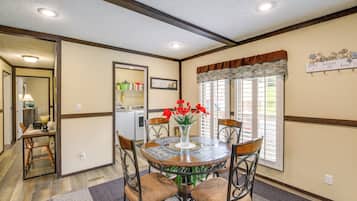 A dining area with a round table, chairs, and a vase with red flowers. There is a window with blinds and a sign on the wall.