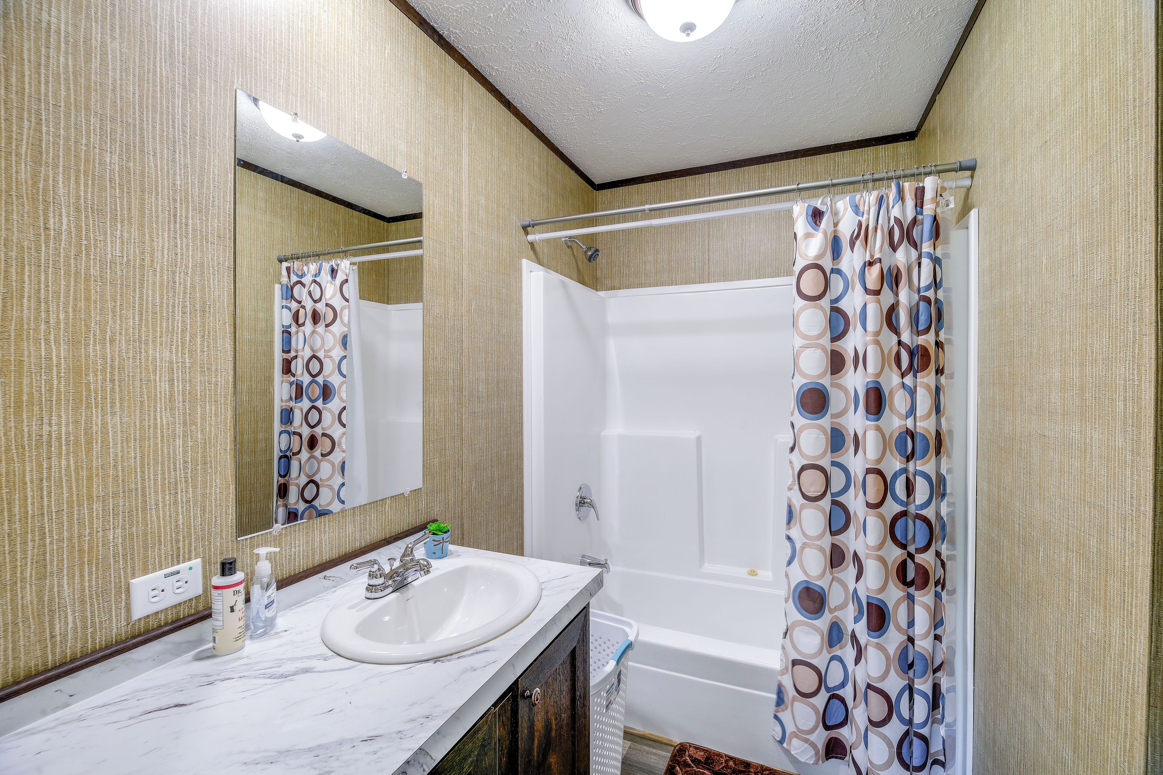 A bathroom with a white bathtub, a sink with a marble countertop, and a shower curtain with a circular pattern.