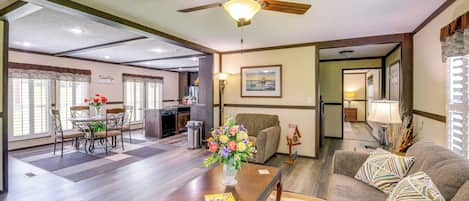 A spacious living room with a dining area, a ceiling fan, a coffee table with a vase of flowers, and a couch with patterned pillows.