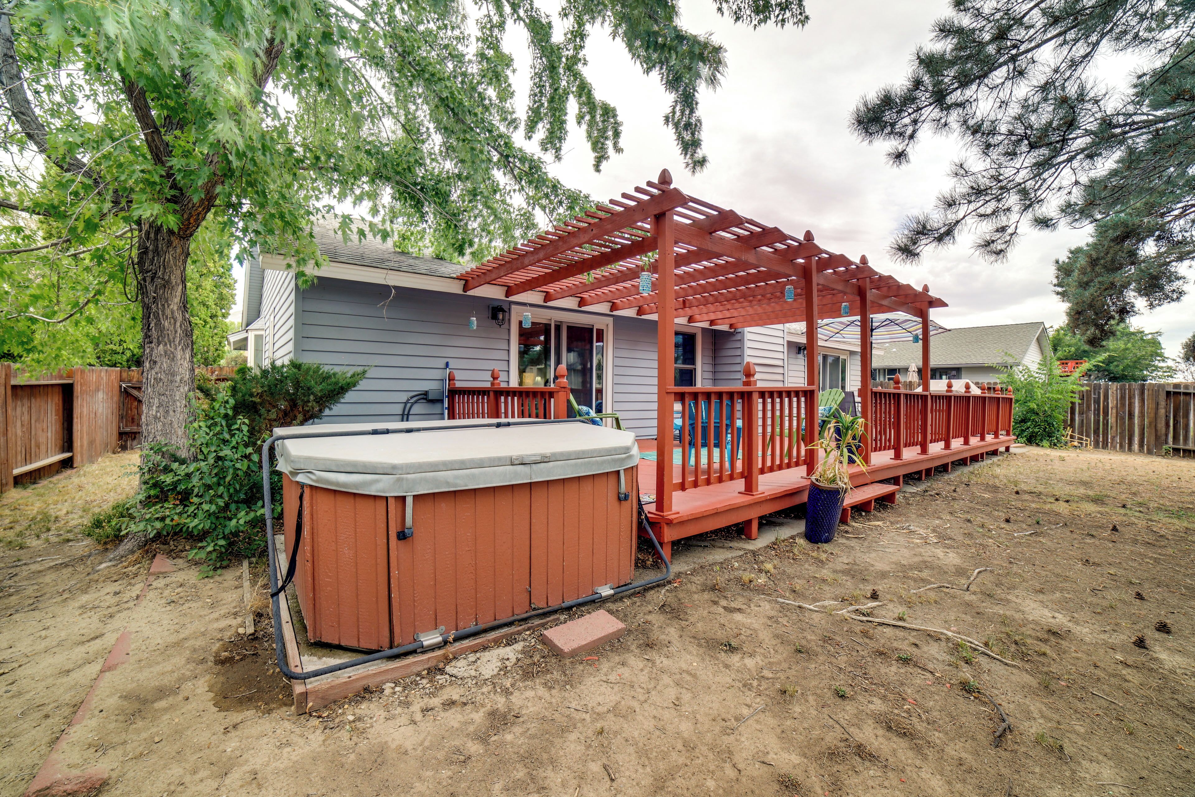 A backyard with a hot tub, wooden deck, and a pergola.