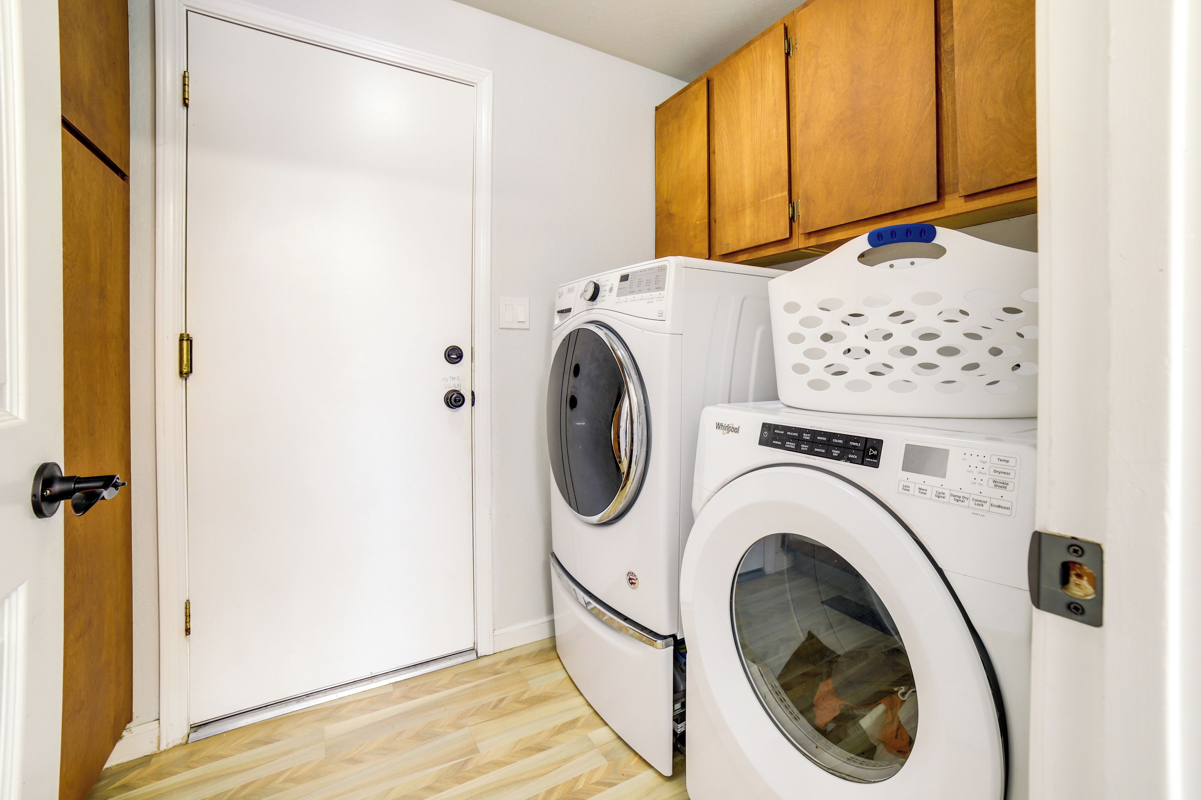 A laundry room with two front-loading washers and dryers, wooden cabinets above, and a white door.