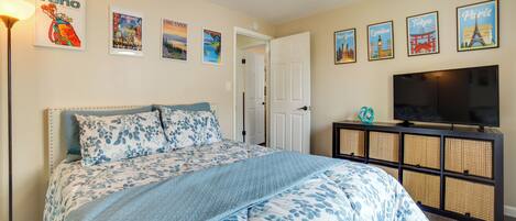 A bedroom with a large bed, a television on a stand, and wall art depicting various cities.