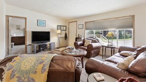 Ein Wohnzimmer mit Fernseher, Ledersofas, einem Couchtisch und einem Fenster mit Jalousien.
