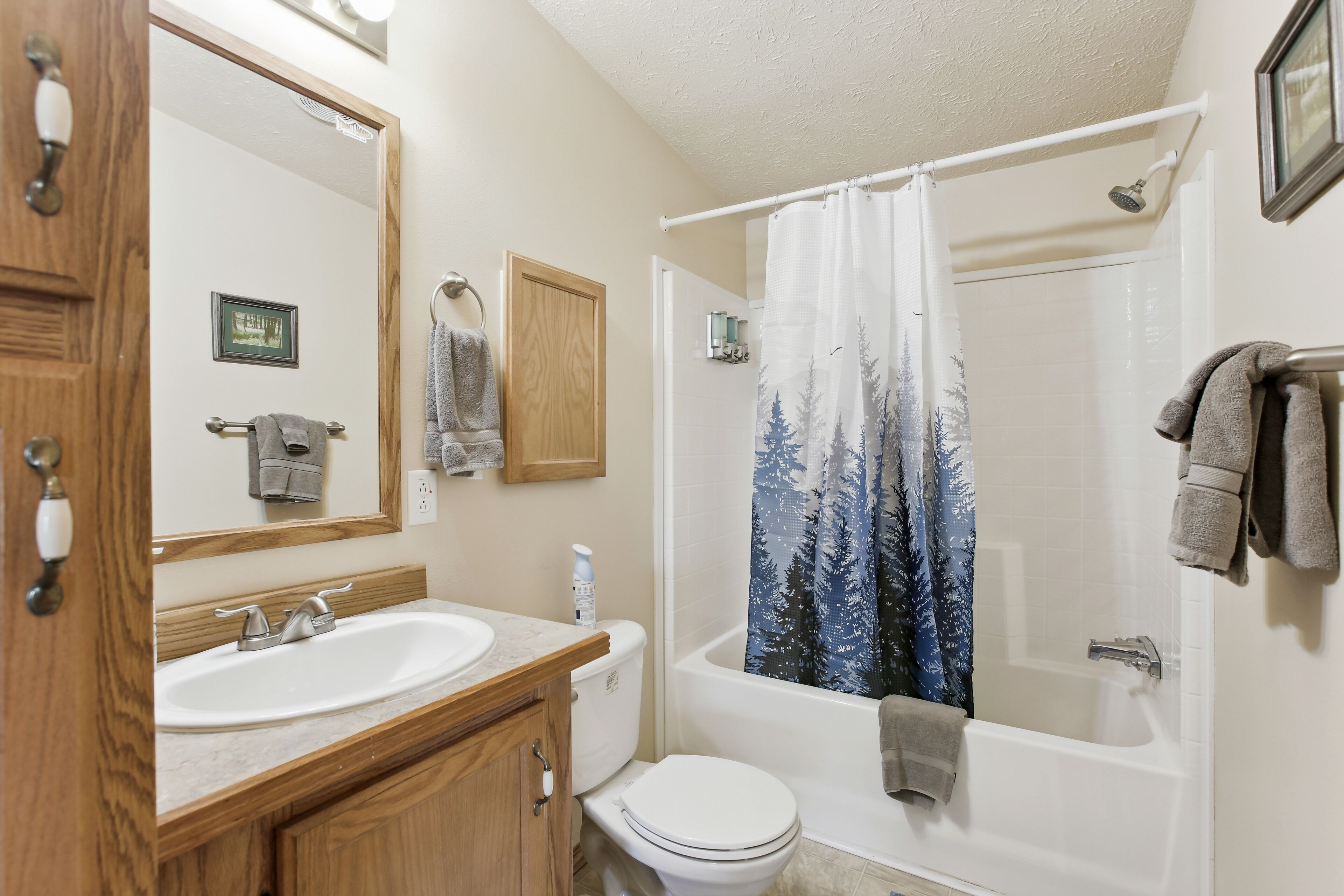 A bathroom with a wooden vanity, a white sink, a toilet, and a bathtub with a shower curtain.