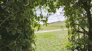 Blick durch einen hölzernen Bogen, der auf eine grüne Wiese und eine entfernte Hügelkette führt.