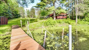 A wooden dock leading into a pond with a house in the background surrounded by trees. - Grill & Fire Pit: Waterfront Cameron Retreat! (Cameron)