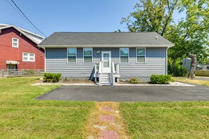A single-story house with a gray exterior, a front porch, and a driveway leading to the entrance. - Charming Edgemere Home w/ Deck & Grill! (Edgemere)